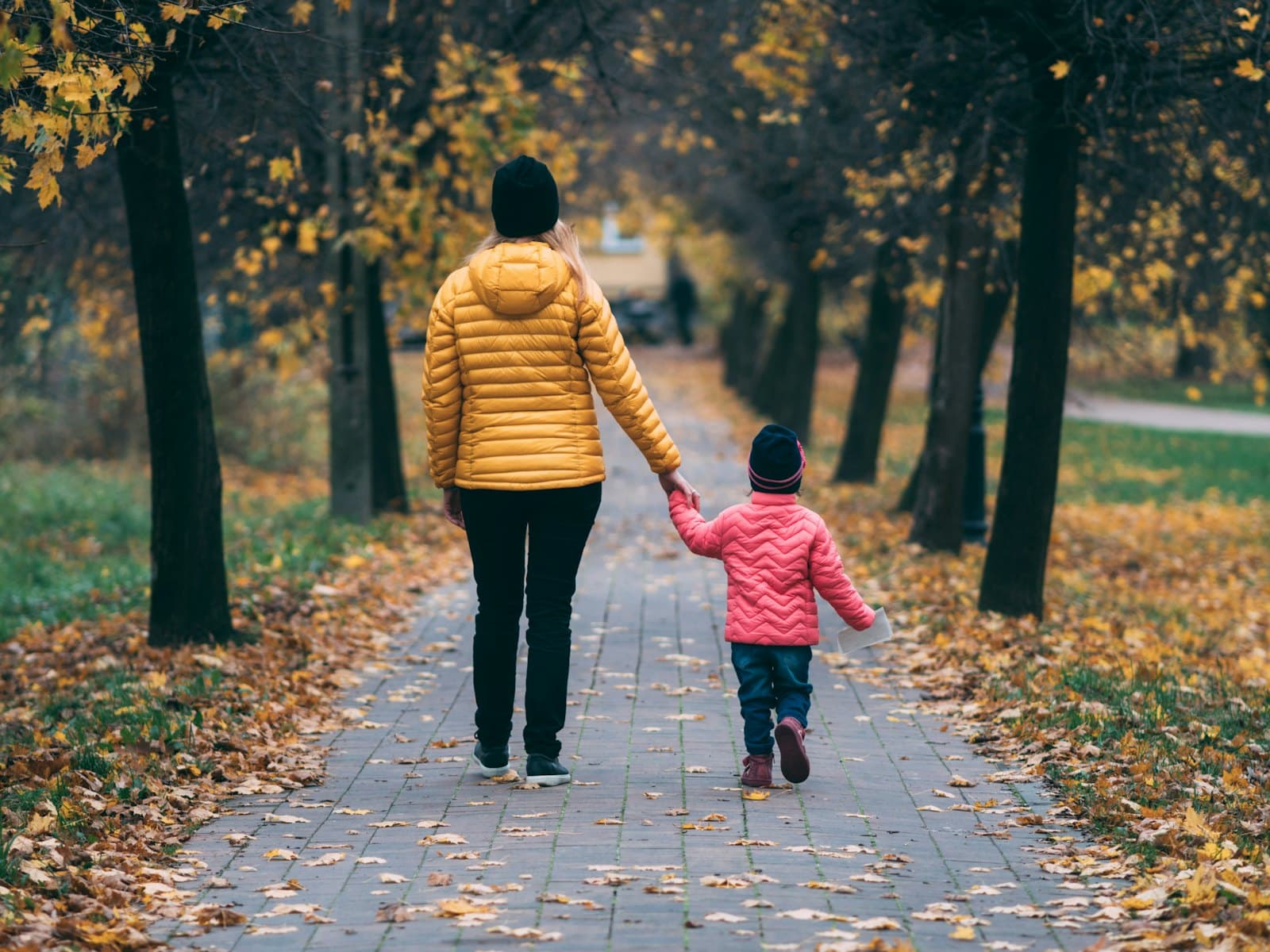 A parent and child walking together along a tree-lined path